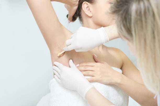 Client with raised arm receiving a waxing treatment at the salon Client with raised arm receiving a waxing treatment at the salon