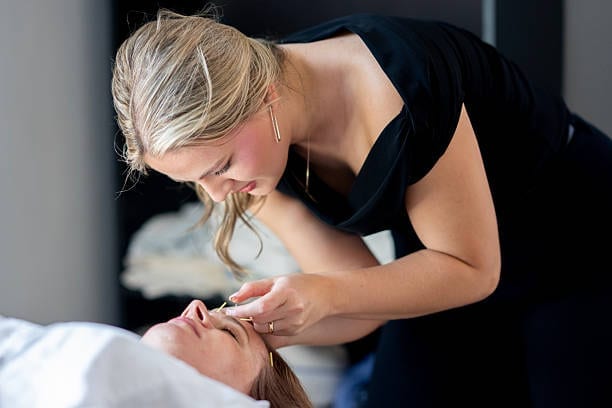 Beautician shaping a client's eyebrows with thread Beautician shaping a client's eyebrows with thread